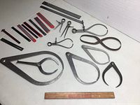 Photo of assorted metal calipers, dividers, and rulers arranged on a white surface with a wooden Coca-Cola ruler for scale.