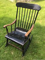Front angled view of black wooden rocking chair with natural wood armrests set on grass.