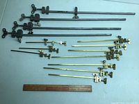 Full view of four long steel clamps and eight brass clamps laid out with wooden ruler for scale.