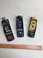 Three Stanley block planes in black, silver and yellow finishes placed above a vintage wood ruler for scale