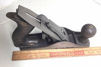 Side view of Stanley No. 3 hand plane with front and rear wooden handles, metal body, and measuring ruler alongside for scale.