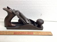 Side view of the Stanley Bailey No.4 Type 9 hand plane showing the wood handle and front knob next to a ruler for scale.