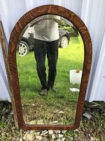 Front view of wooden framed mirror standing outside showing reflective glass and wood grain frame