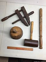 Lot overview showing four wooden tools: clamp, large rounded mallet, lignum vitae mallet, billy club alongside a wooden ruler for scale.