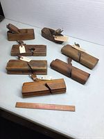 Seven assorted vintage wooden planes for woodworking with various moulding profiles, displayed on white surface with measuring ruler for scale.