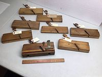 Eight wooden planes arranged on table with ruler for scale