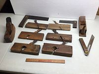 Image showing collection of wooden hand planes, two brass trimmed squares, and a folding wooden measuring tool, laid out on a white surface.