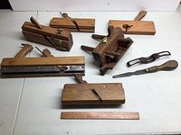 Overview of assorted wooden planes, cast iron spokeshave, and screwdriver on white surface with ruler for scale.