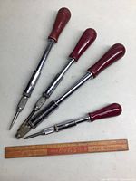 Four Stanley Yankee hand drills with red handles and metal shafts arranged on a white surface next to a vintage Coca-Cola wooden ruler for size reference.