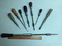 Full set laid out on table, showing eight drills and screwdrivers of various sizes and handle colors and materials beside a ruler for scale