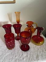 Photo showing all 7 glassware items in red and amberina hues on a white textured surface.