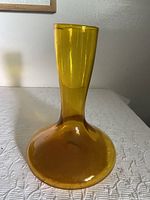 Front view of the gold glass vase showing its flared base and tall narrow neck on a white textured surface.