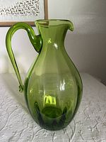 Green Blenko glass pitcher front angled view showing spout, handle and bulbous optic swirl body.