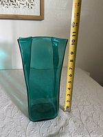 Tall blue-green Blenko glass vase shown with measuring tape showing about 11 inches height.