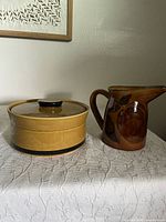 Stoneware casserole dish with lid and glazed brown fruit motif pottery pitcher side by side.