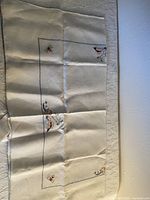 Full view of embroidered linen tablecloth with boat and wave motifs in multiple colors on off-white linen fabric