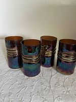 Four iridescent glasses with amber interiors and textured dark iridescent exteriors with horizontal ridges.