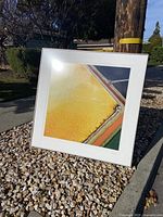 Framed abstract picture outdoors showing mainly yellow area with geometric shapes and textured pattern.