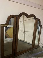 View of the front side of a large oak dresser mirror with three mirrored panels and a decorative curved top frame.