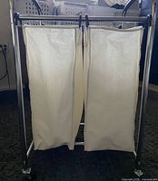Front view of the laundry sorter showing two vertical white fabric bags and the black metal frame on wheels.
