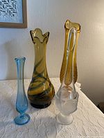 Four swung glass vases of varying shapes and colors arranged on a white cloth surface, showing the lot contents.