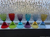 All six reversible crystal glasses shown aligned side by side with window background highlighting colors. Colors include red, green, blue, purple, and yellow. The glasses show upside-down and right-side-up designs.