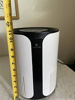 Front view of Medify Air Purifier showing white body with black center panel and top control panel with measuring tape showing height approximately 12 inches.
