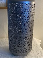 Metal table lamp with detailed cutout pattern on a cylindrical body, placed on a white surface.