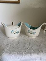 Frontal view of matching creamer and sugar bowl with floral design and turquoise interiors