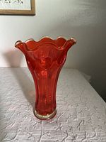 Full view of the red Viking Glass ruffle top thumbprint vase on a white textured surface.