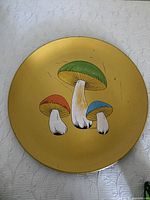 Circular yellow mushroom tray with painted green, red, and blue mushroom caps, showing surface scratches and wear.