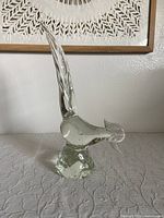 Front angle photo of clear Murano glass bird sculpture showing lengthened tail and rounded textured base.