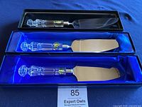 Three Waterford servers displayed in original blue satin-lined boxes on dark surface, showing cut crystal handles and stainless steel blades with Waterford green labels.