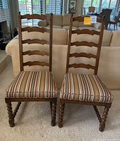 Front view of two antique wooden chairs showing ladder back design and striped upholstered seat cushions.