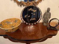 Photo showing all four Asian themed items arranged on a wooden table under a mirror: bowl, lacquered tray, terracotta warrior figurine, and carved frame.