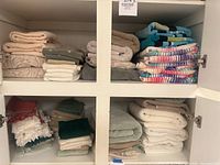Two shelves with stacks of bath towels, hand towels, and washcloths in cream, beige, grey, sage, and multicolor stripes.