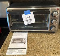 Black & Decker toaster oven on kitchen counter with instruction manual in front. Oven front glass door has label with lot number.