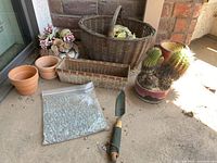 Photo showing cactus in southwest decorated ceramic planter, terra-cotta small planters, wicker baskets, gardening shovel, clear glass marbles/pebbles bag