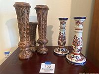 Photo of two carved wood candlesticks with wheat motifs and two ceramic candlesticks with painted lotus flowers