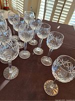 Twelve clear crystal glasses arranged on a brown surface, showing diamond cut pattern with no visible chips.