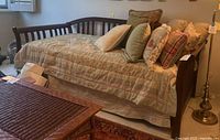 Day bed from front angle showing dark wood frame with multiple pillows and quilt.