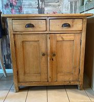 Front view showing two drawers with black metal cup handles and double paneled cabinet doors with round metal knobs and a keyhole.