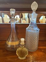 Photo showing all three items on a wooden surface with mirror background: two glass decanters and one seashell-shaped whiskey bottle