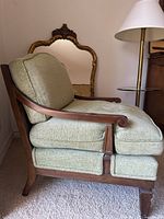 Side angle view of mid century vintage accent chair showing wooden armrest with curved scroll detail and sage green herringbone fabric upholstery.