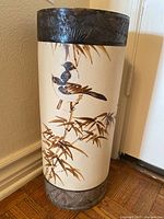 Full view of ceramic umbrella stand with painted birds on bamboo and metal bands with leaf embossing on top and bottom.