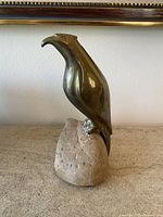 Front view of brass bird sculpture perched on stone base