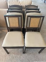 Eight chairs stacked and unfolded showing rattan backs and cream seats