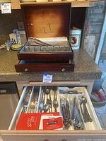 Wooden large flatware organizer box with lined lid open and drawer open showing assorted flatware including spoons, forks, knives.