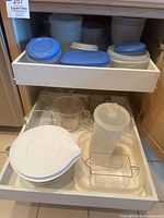 Drawer with Rubbermaid white plastic containers with blue lids, Tupperware pitcher, and Pyrex glass measuring cups and mixing bowl