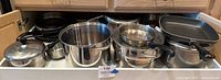 Overview of the pots and pans inside a cabinet showing various sizes and types, including stainless steel pots, Calphalon sauté pans, and grill pan.